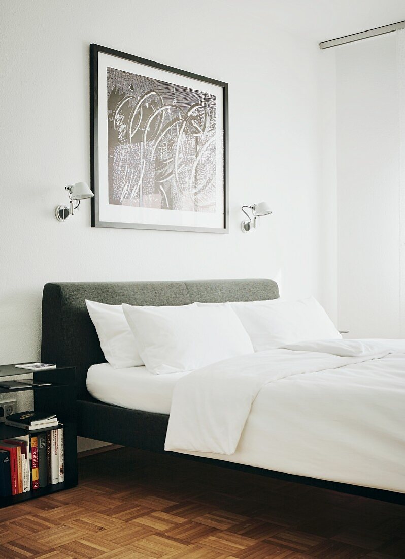 Double bed with grey upholstered headboard, white bed linen and Tolomeo wall lamps flanking framed picture