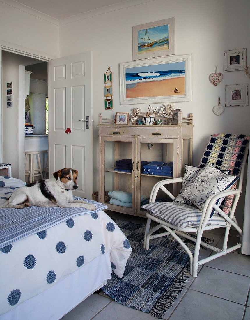 Dog on bed, white bamboo chair with cushions and cabinet with glass doors in rustic-maritime bedroom