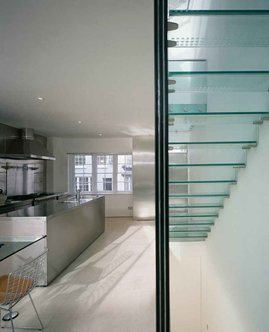 Treppe mit Glasstufen in offener Küche mit Küchenblock aus Edelstahl