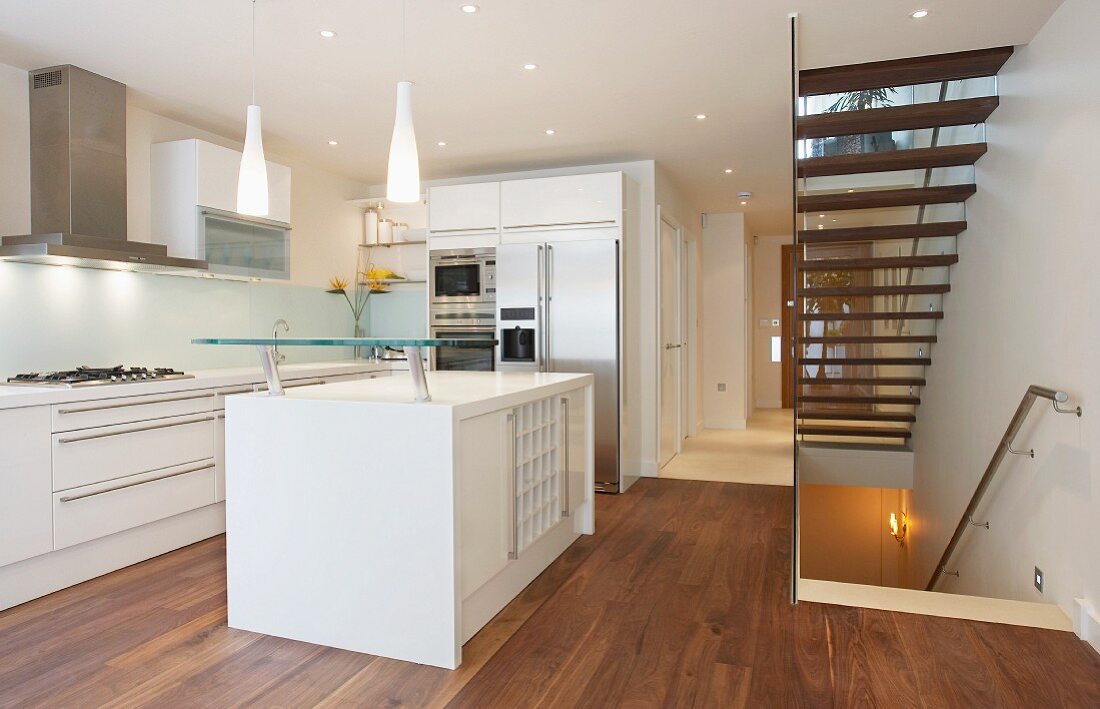 Offene Küche mit weißem freistehendem Küchenblock auf Nussbaumdielenboden und offenem Treppenhaus