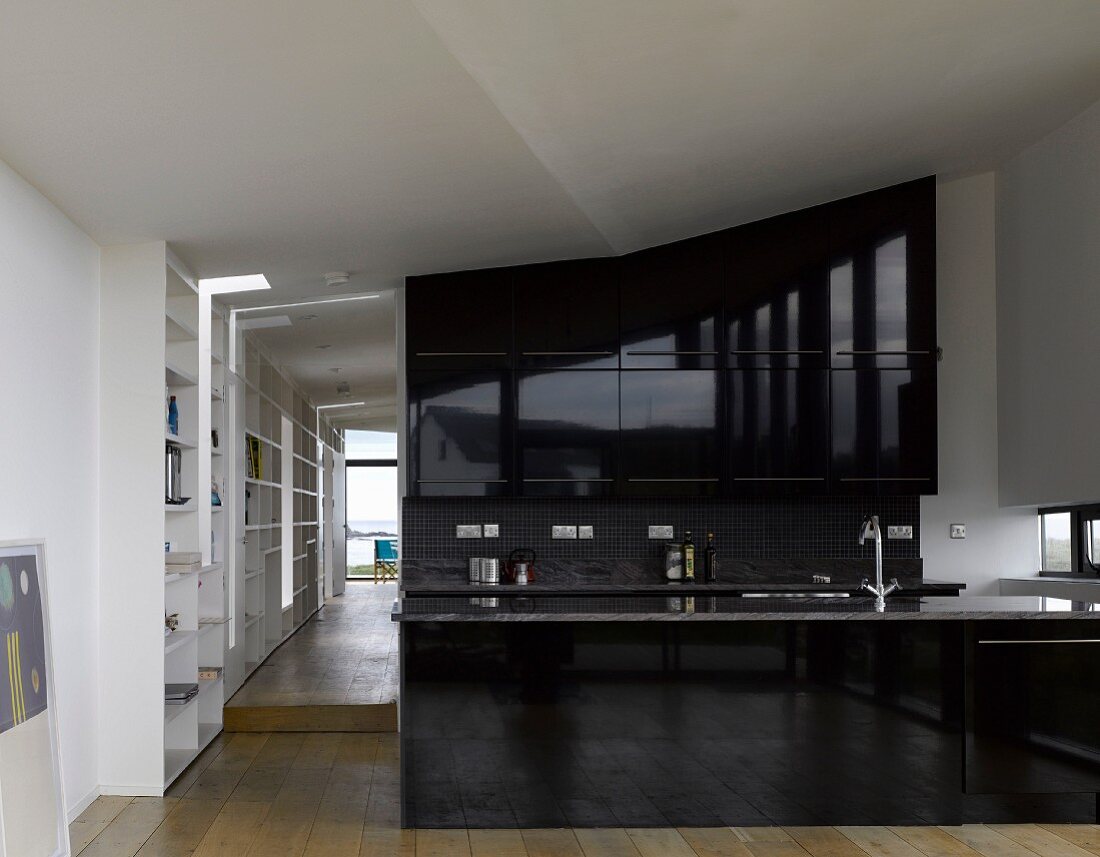 Offene Küche mit schwarzen hochglänzenden Fronten in loftartiger Wohnung und Blick durch offenen Gang