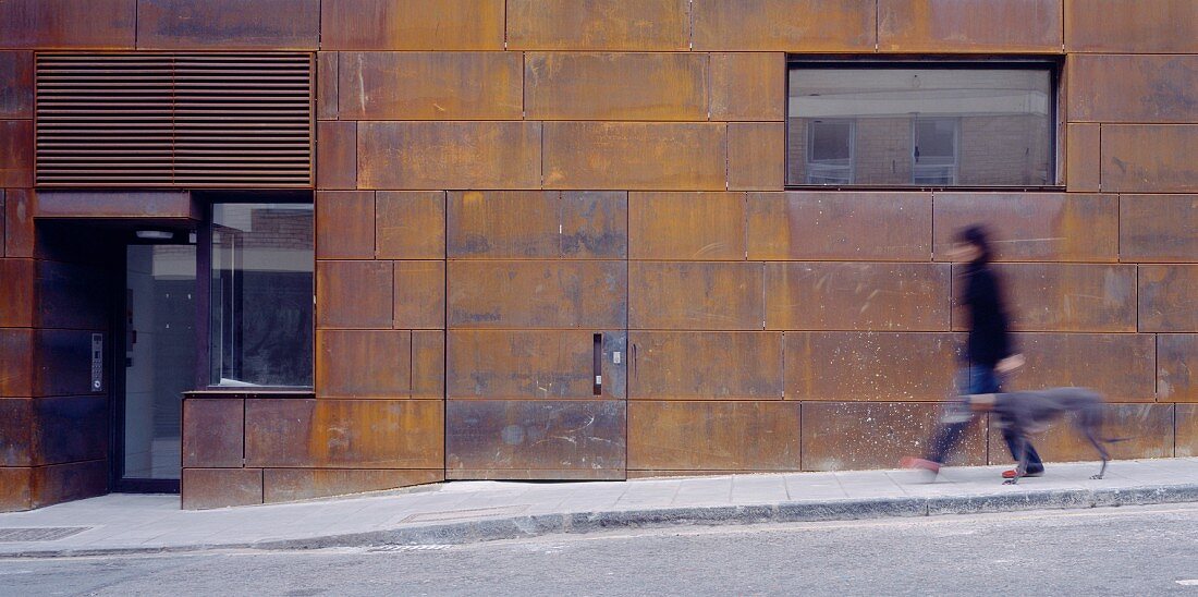 Man taking a dog for a walk in front of a house facade with rusty Corten steel siding