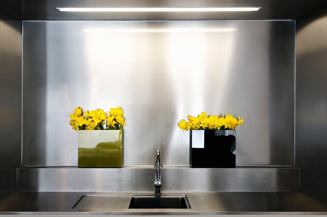 Sink in front of a wall niche clad in stainless steel and yellow flowers in vases