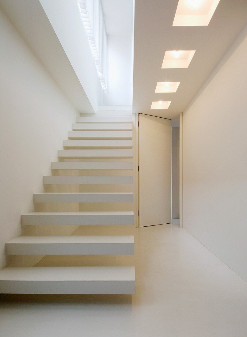 Designer staircase in white with protruding steps, above, a ceiling cut out with lights