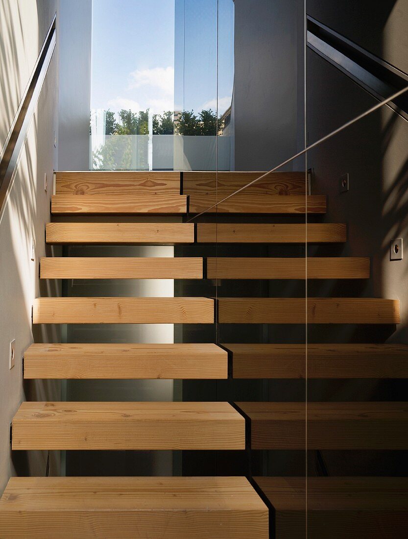 Schmales Treppenhaus mit offenen Holzstufen und schwarzen Steinfliesen an Wand