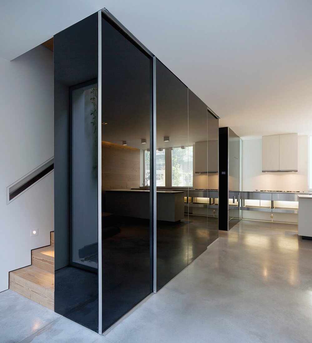 Black, high-gloss built in cupboard in the hallway in front of staircase on a polished concrete floor