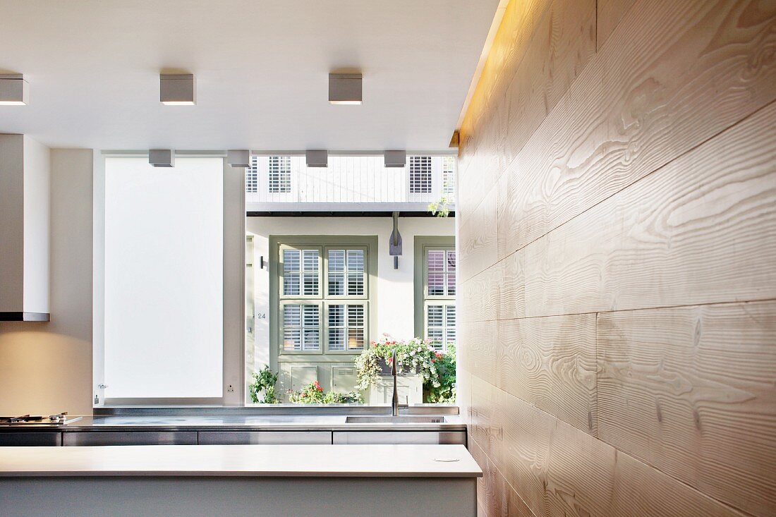 Offene Küche neben holzverkleideter Wand und Blick durch Fenster auf Nachbarhaus