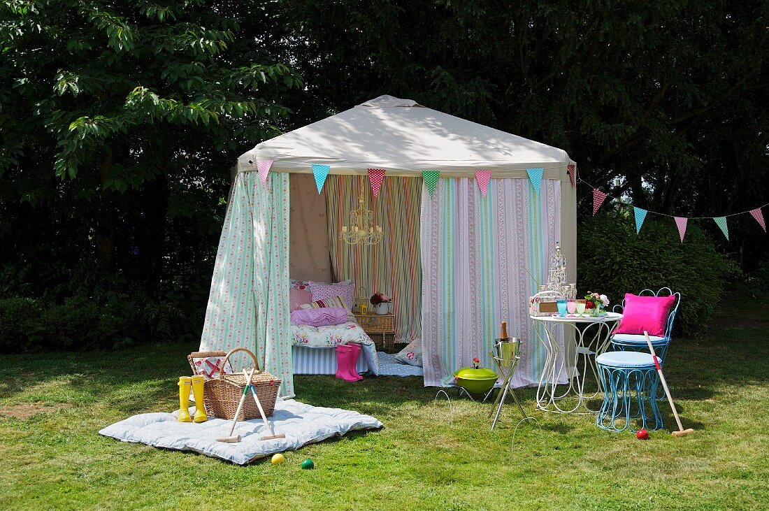 Gartentisch mit Stuhl, Decke mit Picknickkorb und Croquet vor einem grossen Zelt mit Bett