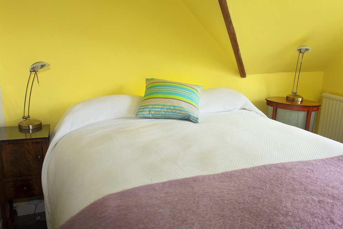 A double bed in a yellow painted attic bedroom