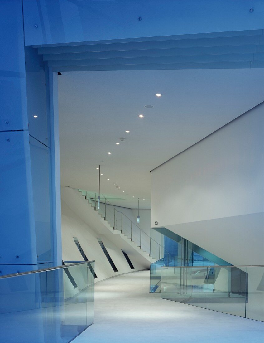 Gallery with glass balustrade and staircase in large foyer with slanting components and ceiling spotlights
