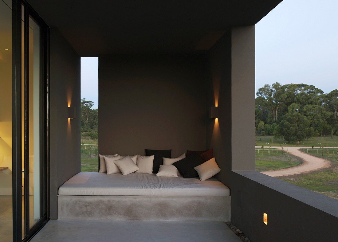 Terrace of South American house with cushions piled on concrete couch and protected by dark-grey wall elements