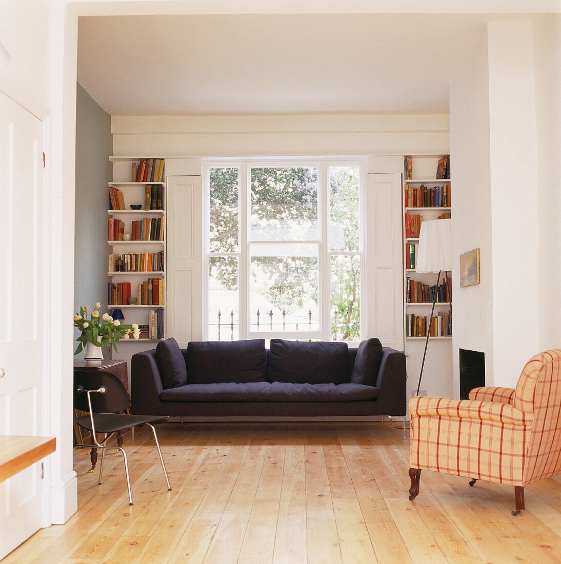 Schwarzes Sofa unter Fenster und antiker Sessel mit kariertem Bezug im offenen Wohnzimmer