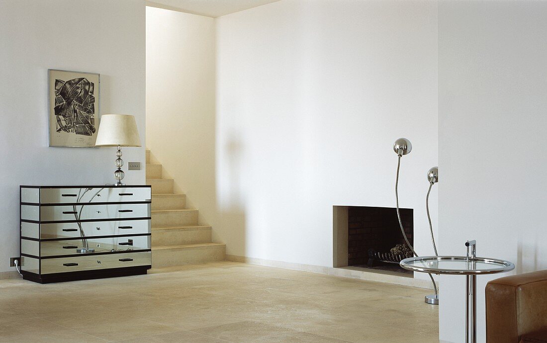 Minimalist living room with designer mirrored chest of drawers beside an open hallway with stairs and side table in Bauhaus style