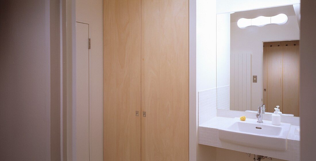 Bathroom with wooden built-in cupboard next to a simple, white wash basin