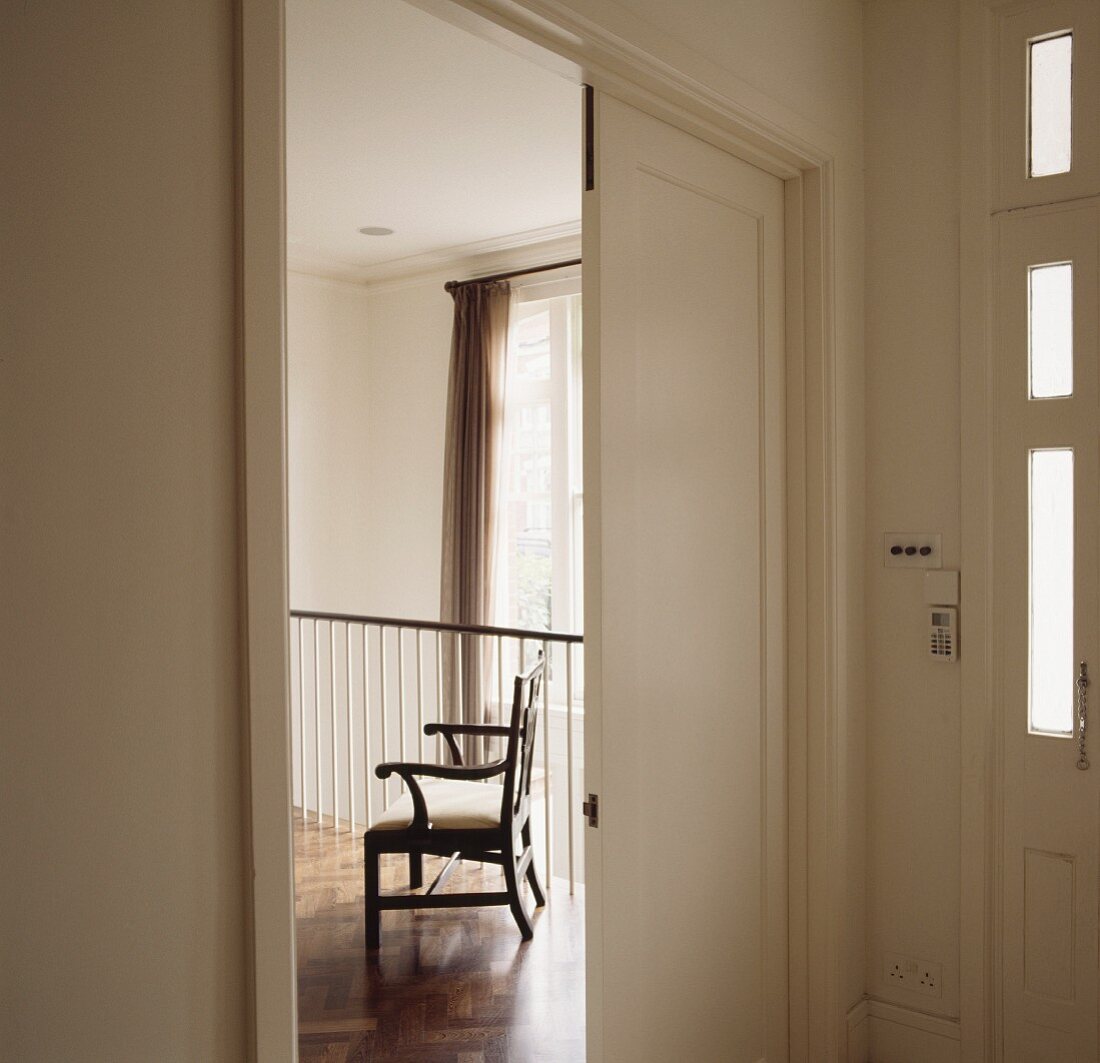 Vorraum mit offenem weissen Türflügel und Blick auf antiken Armlehnstuhl auf Galerie