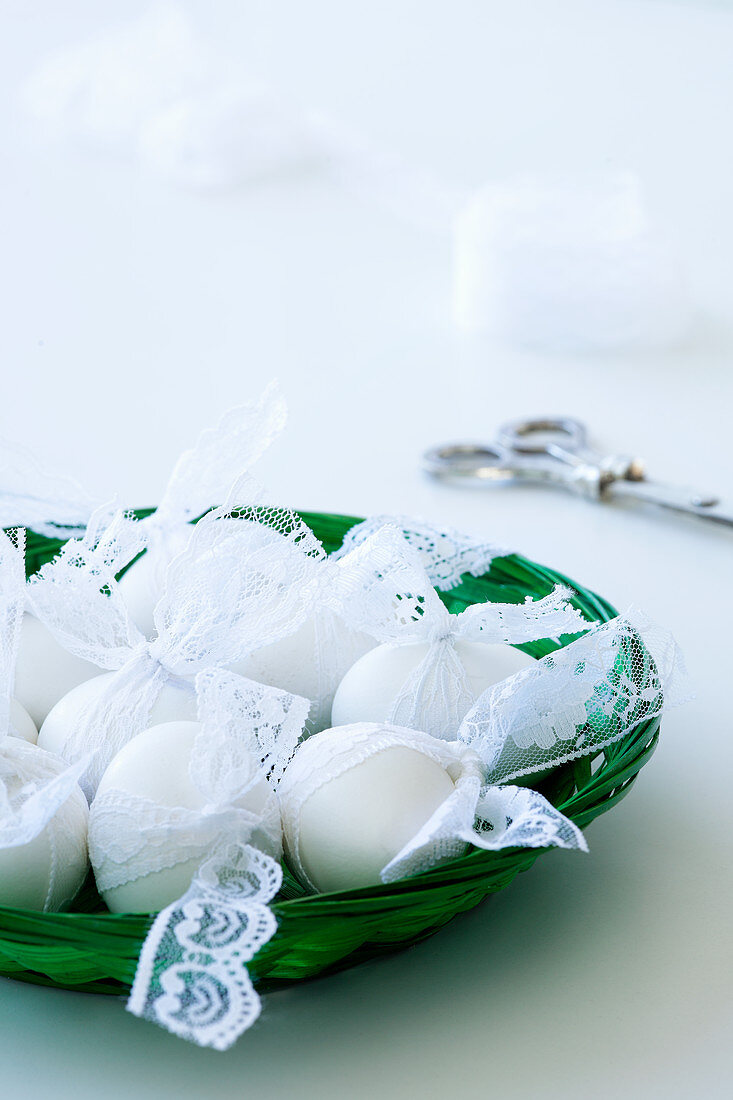 weiße Eier mit Spitzenbändern im Korb