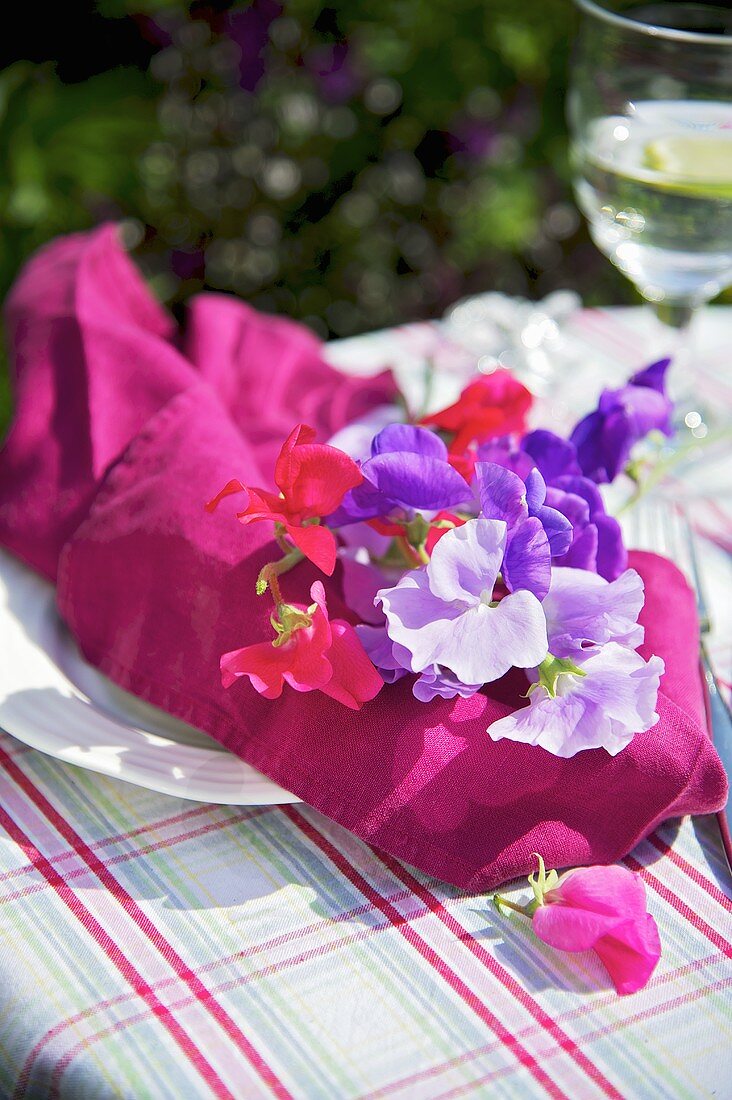 Gedeck mit Stoffserviette und Blumen auf Gartentisch