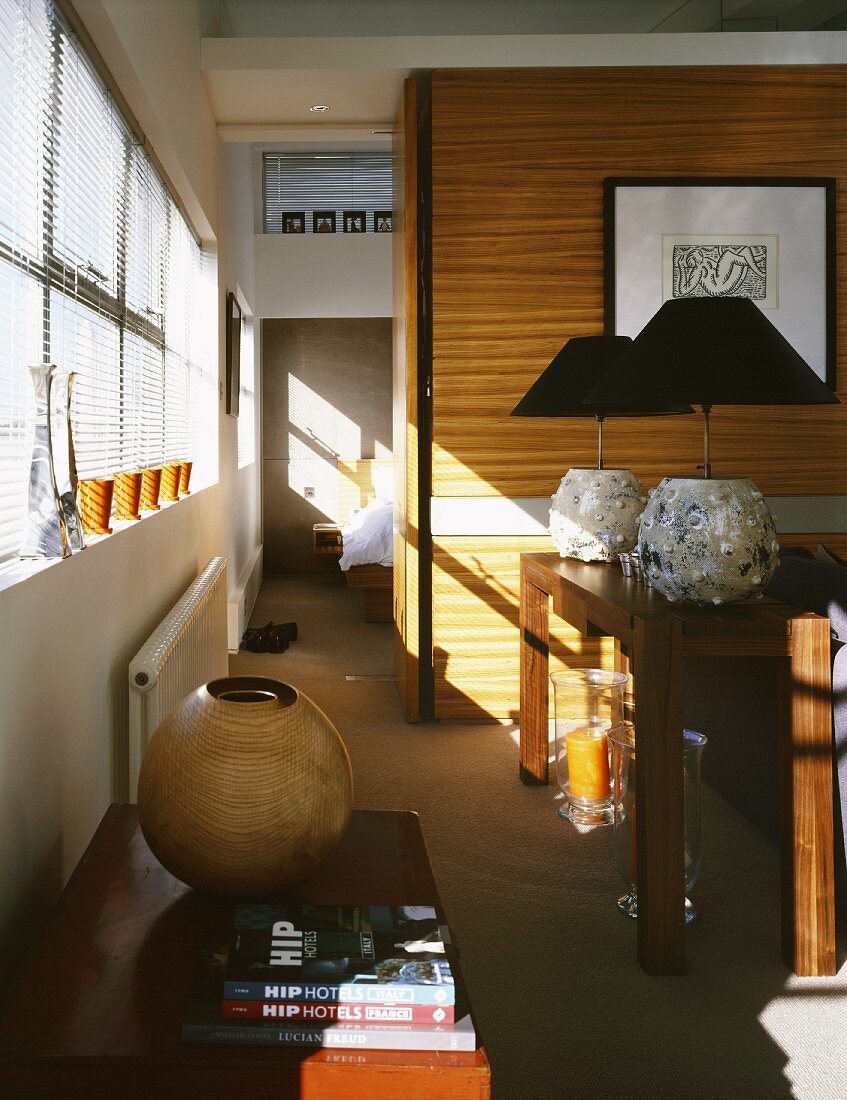Kugelförmige Vase auf Truhe und Tischlampen mit schwarzem Schirm im Esszimmer und Blick durch raumhohen Durchgang