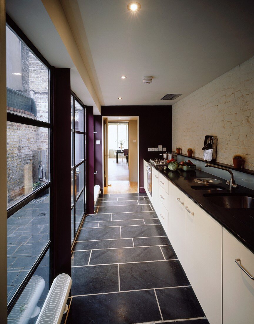 Narrow, galley kitchen with white cabinets under the countertop and grey tiled floor with light colored grouting