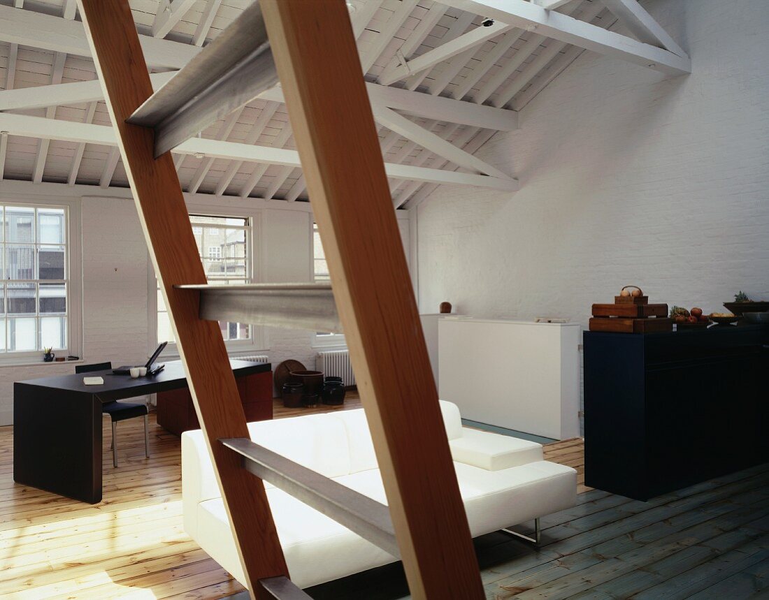 Blick durch Holzleiter in offenen Wohnraum einer ehemaliger Fabrikhalle auf weisses Sofa und Schreibtisch