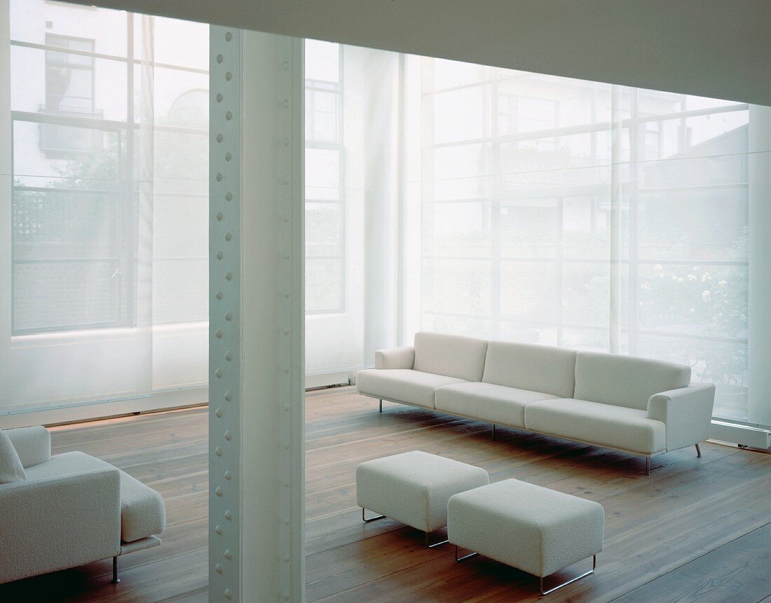 weiße Sofagarnitur und passende Polsterhocker vor transparentem Vorhang am Fenster in ehemaliger Fabrikhalle