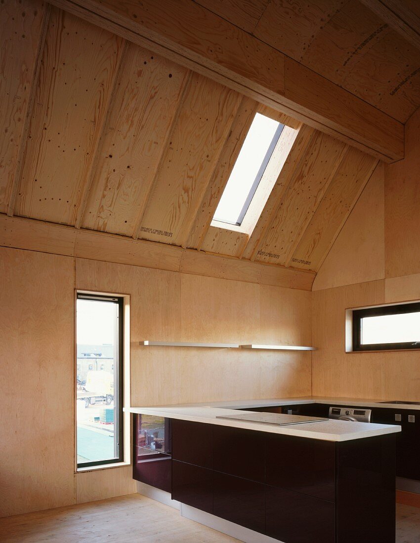 Offene Küche mit Theke und dunkler Holzfront im ausgebauten Dach mit heller Holzverkleidung und verschiedenen Fenstern