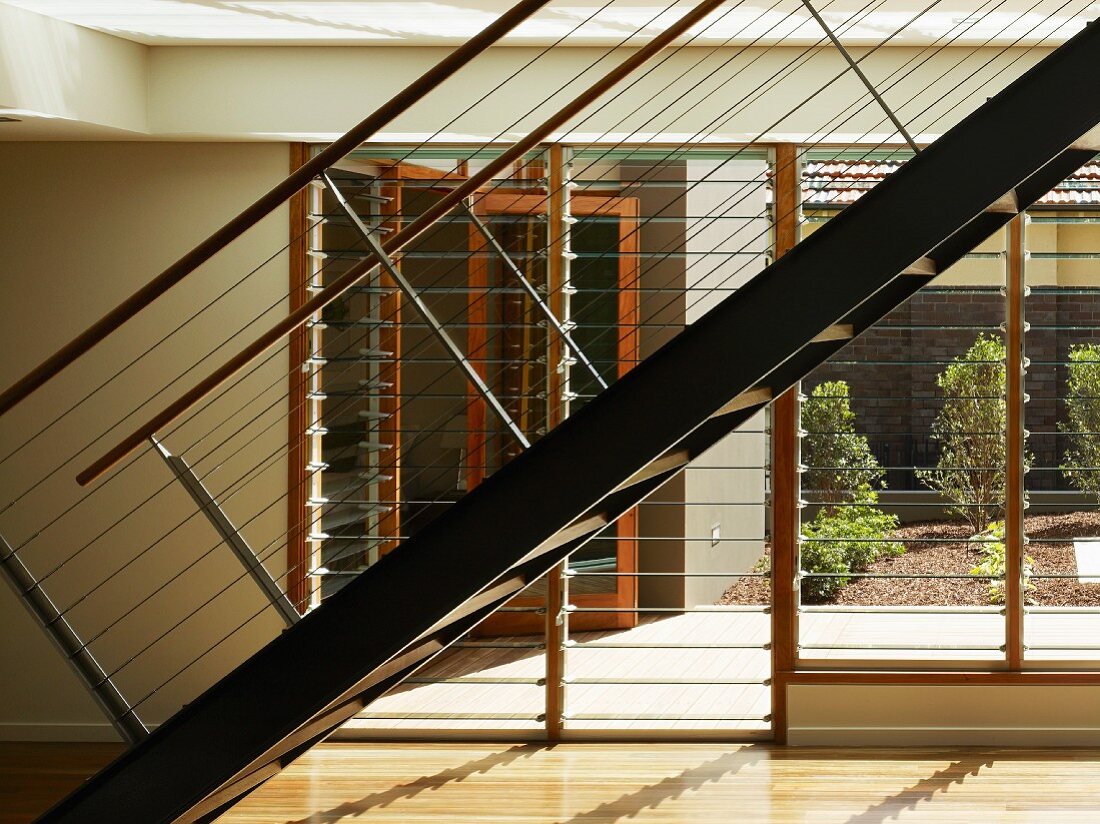 Metalltreppe mit Geländer und horizontalen Drahtseilen vor Fensterfront mit verstellbaren Glaslamellen