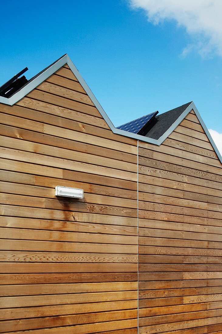 Ausschnitt einer Hausfassade mit Holzverkleidung und Solarzellen auf geneigtem Dach