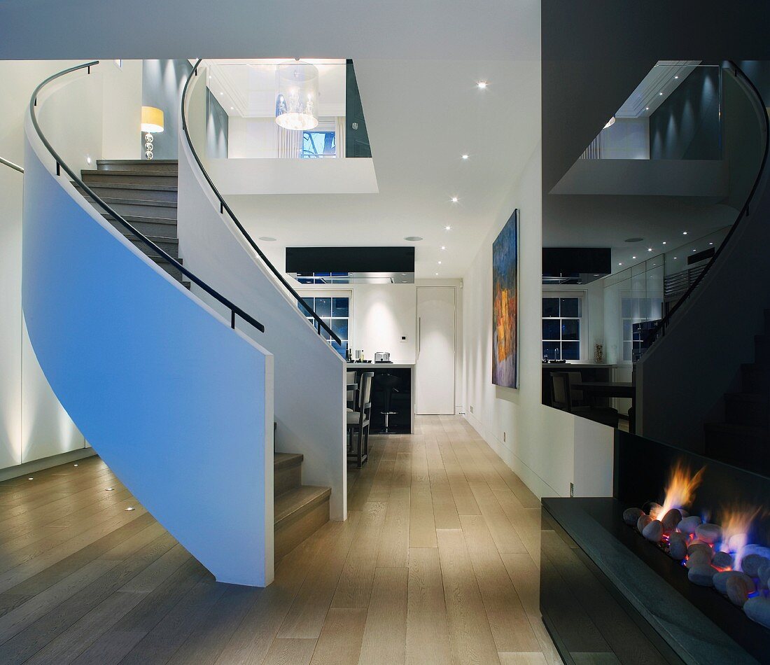 Moderner offener Wohnraum mit geschwungener Treppe und Kaminfeuer