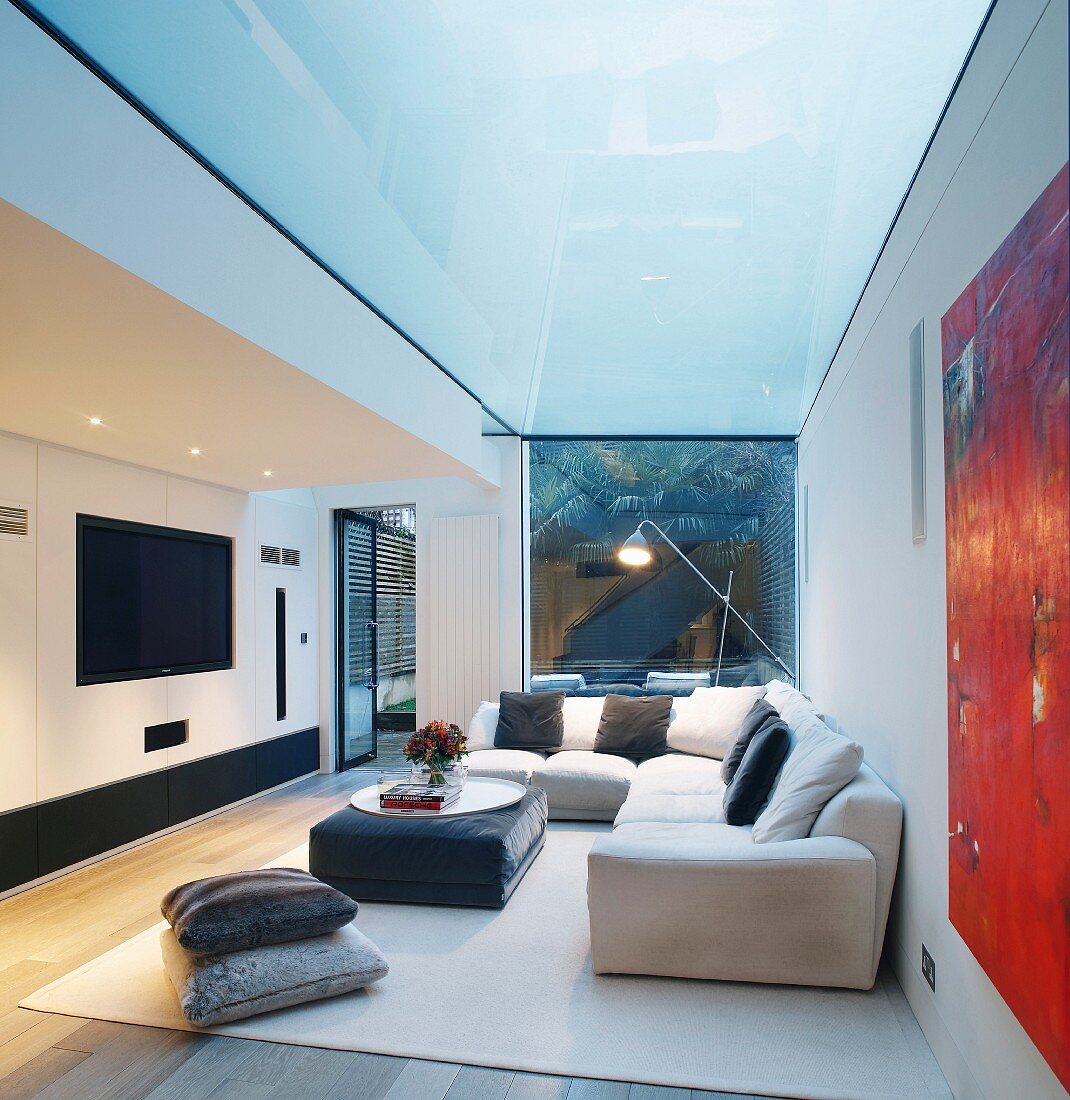 Gemütliche Polstersofaecke mit Kissen im modernen Wohnraum unter verglastem Deckenbereich