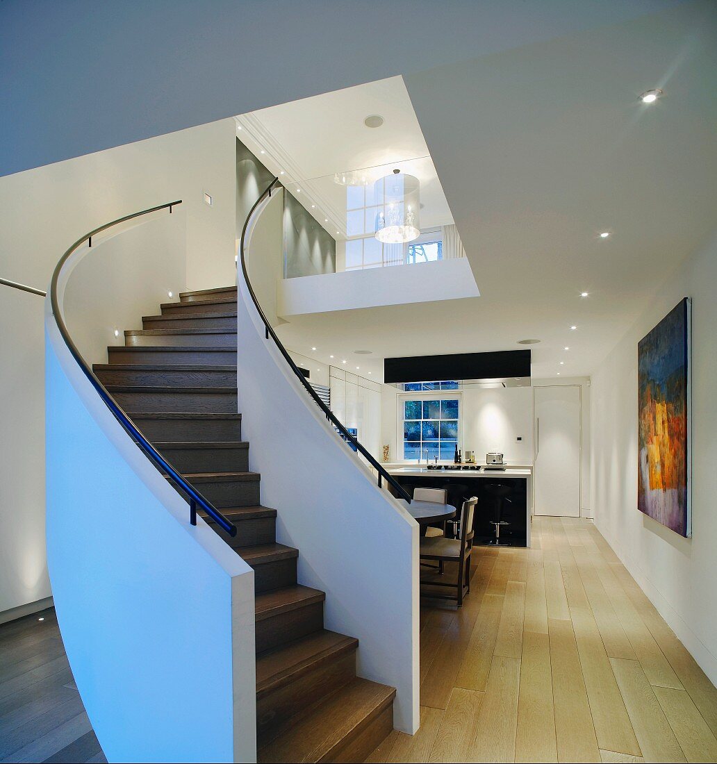 Geschwungene Treppe mit Blick auf Designer Deckenlampe und offenen Küchen/Essraum mit hellem Dielenboden