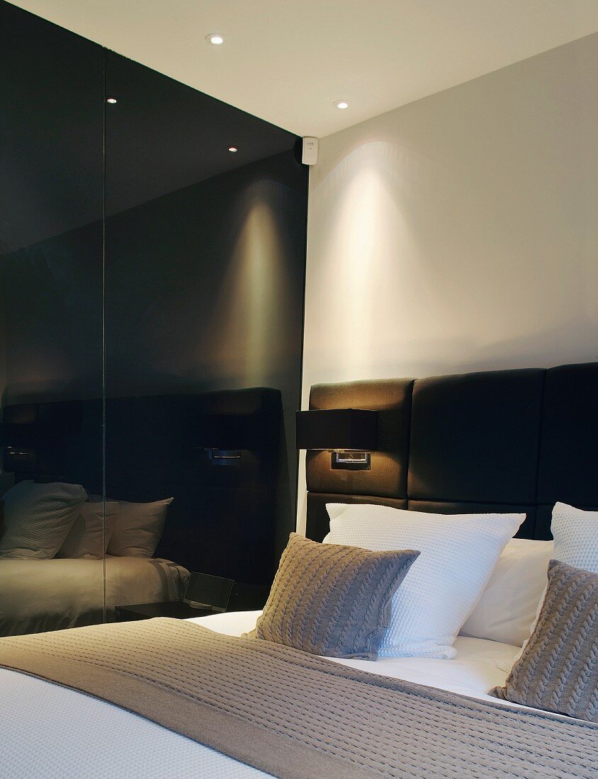 Kissen auf Doppelbett mit gepolstertem Kopfteil und schwarze spiegelnde Wand