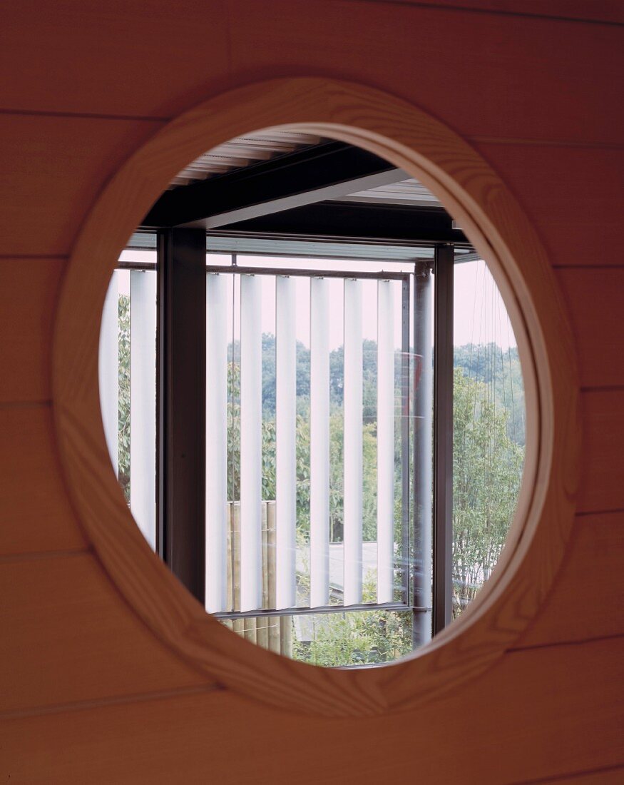 Blick durch Bullauge in Holzfassade auf Fenster mit Lamellen