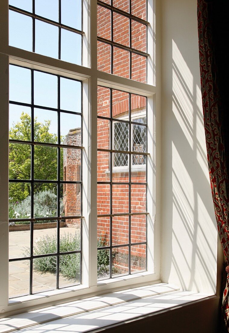 Blick durch Bleiglasfenster auf Haus mit Ziegelfassade und Garten