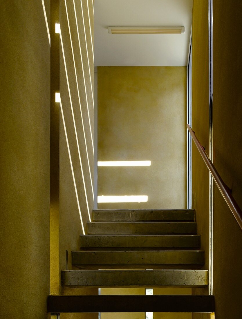 Strip lighting on a yellow wall and concrete steps in a narrow stairway
