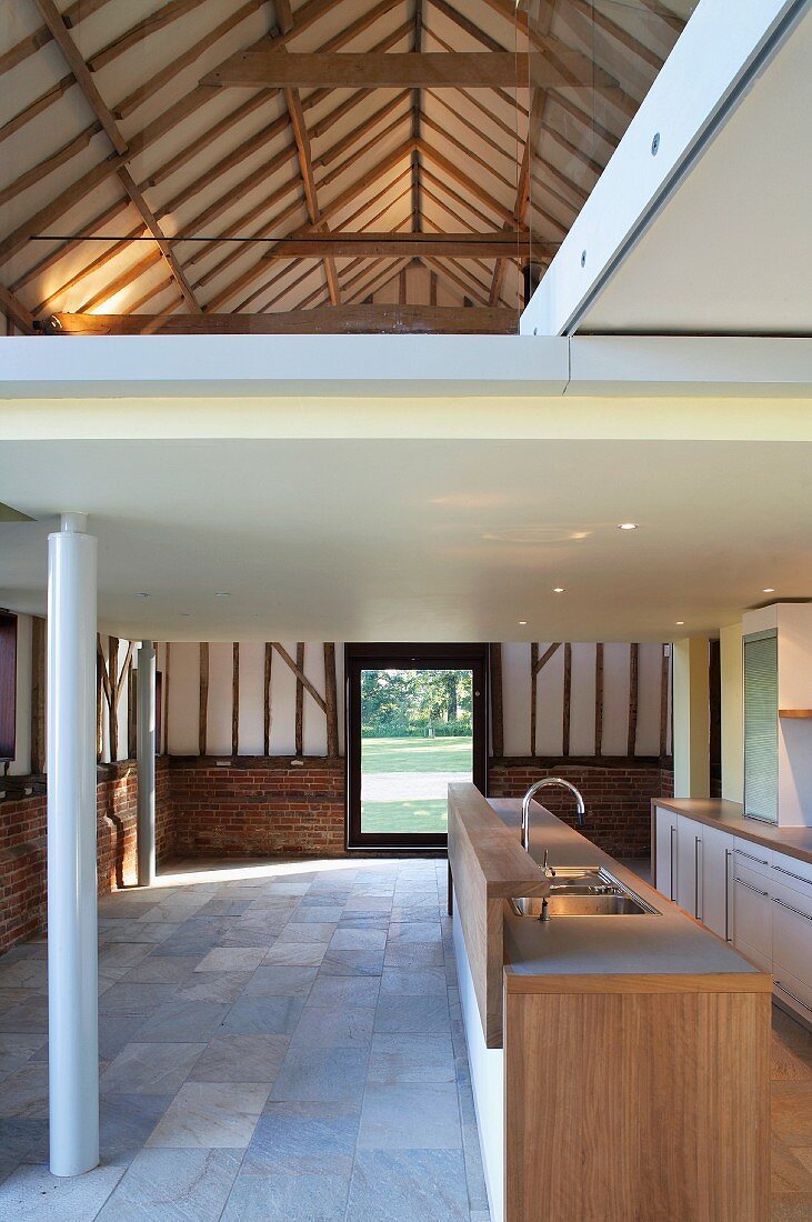 Former barn with freestanding kitchen counter under a mezzanine with white metal supports