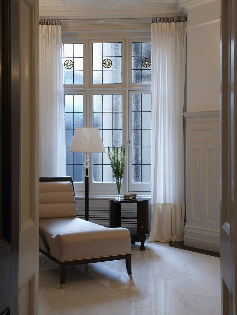 Blick durch offene Tür auf Chaiselongue mit weißem Lederbezug im Art Deco Stil vor Bleiglasfenster