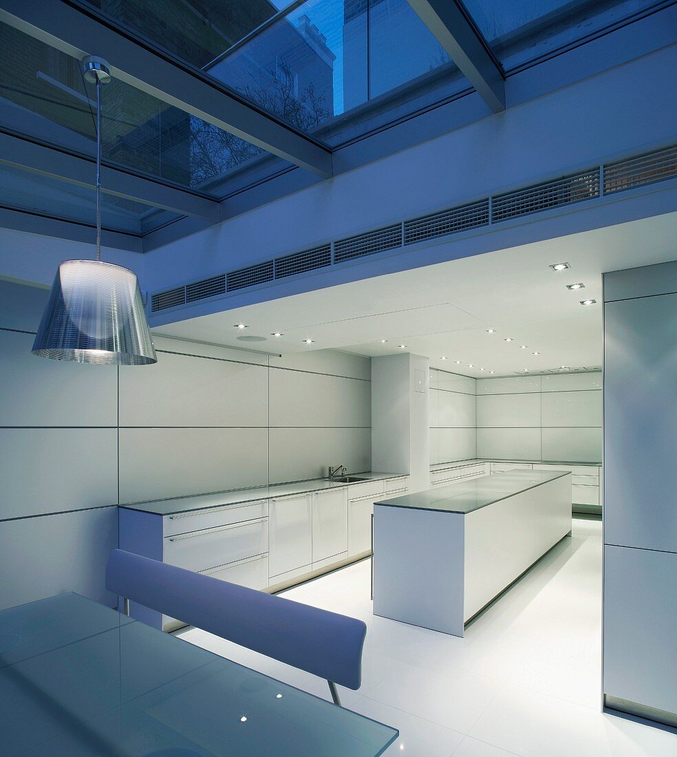 Evening mood in a sunken dining room under a glass ceiling in front of a cool designer kitchen in white