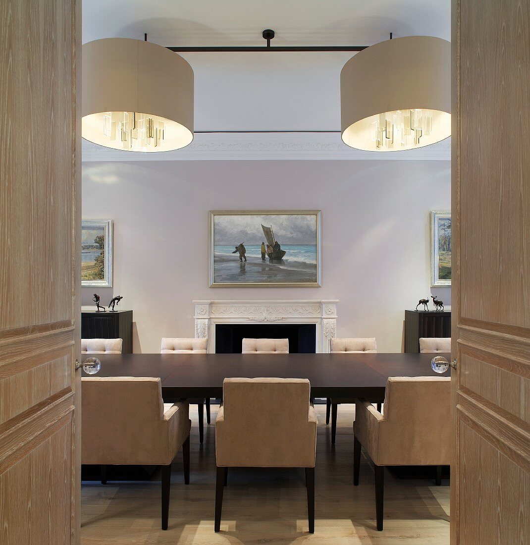 View through open double doors of dining table with upholstered chairs and designer pendant lights in dining room