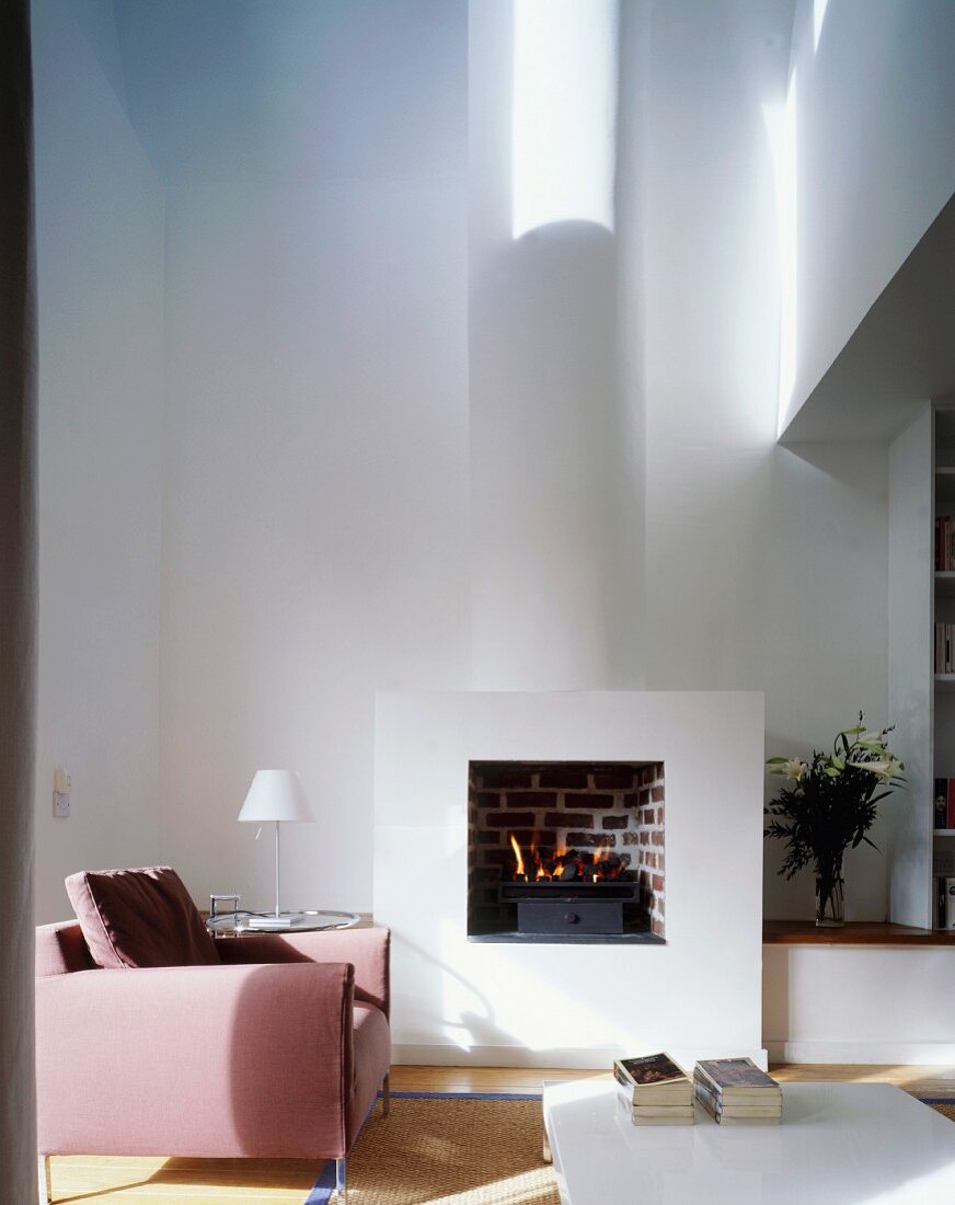 Rosa Sessel vor Kaminfeuer im offenen minimalistischen Wohnraum
