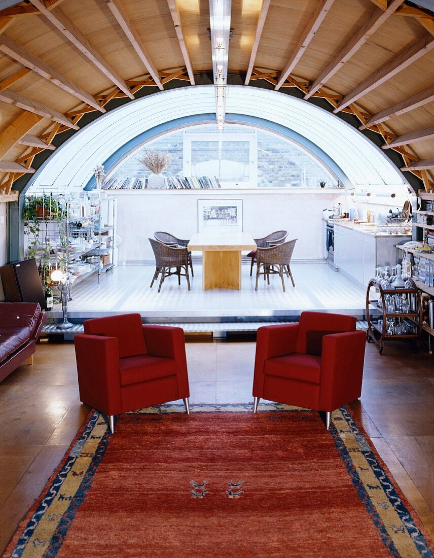 Rote Sessel vor Podest mit Essplatz im offenen Raum unter Tonnendecke