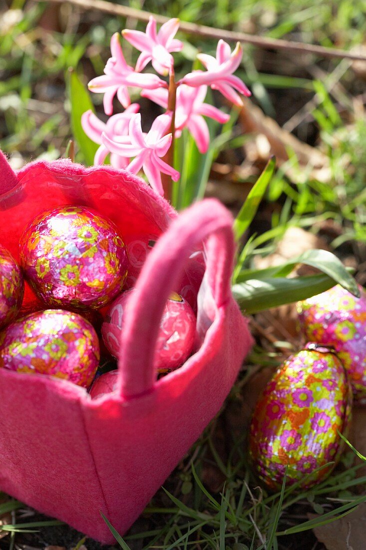 Chocolate Easter eggs in a pink felt basket in a meadow