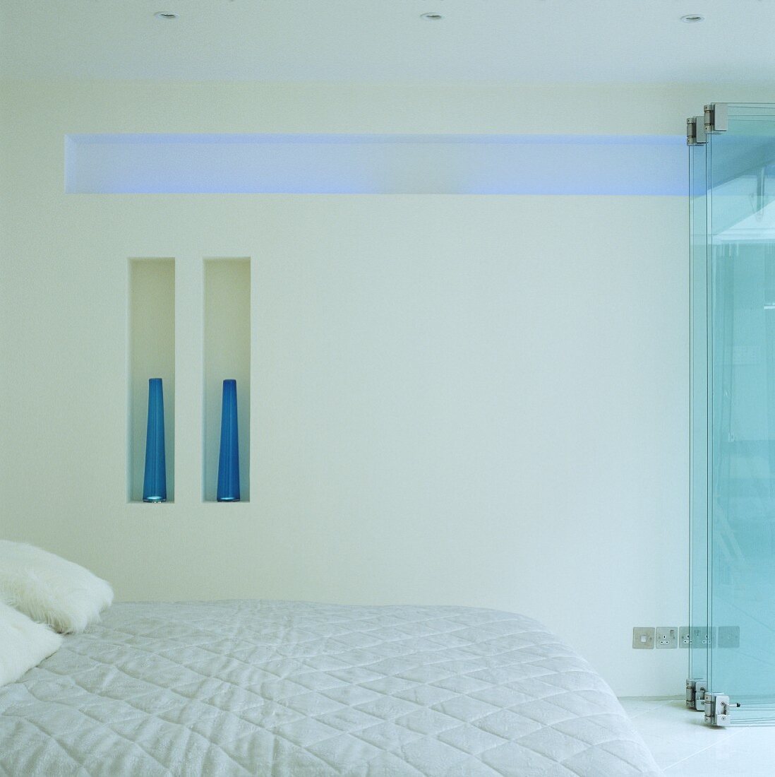 White bedroom with double bed and indirect blue lighting in a horizontal wall niche