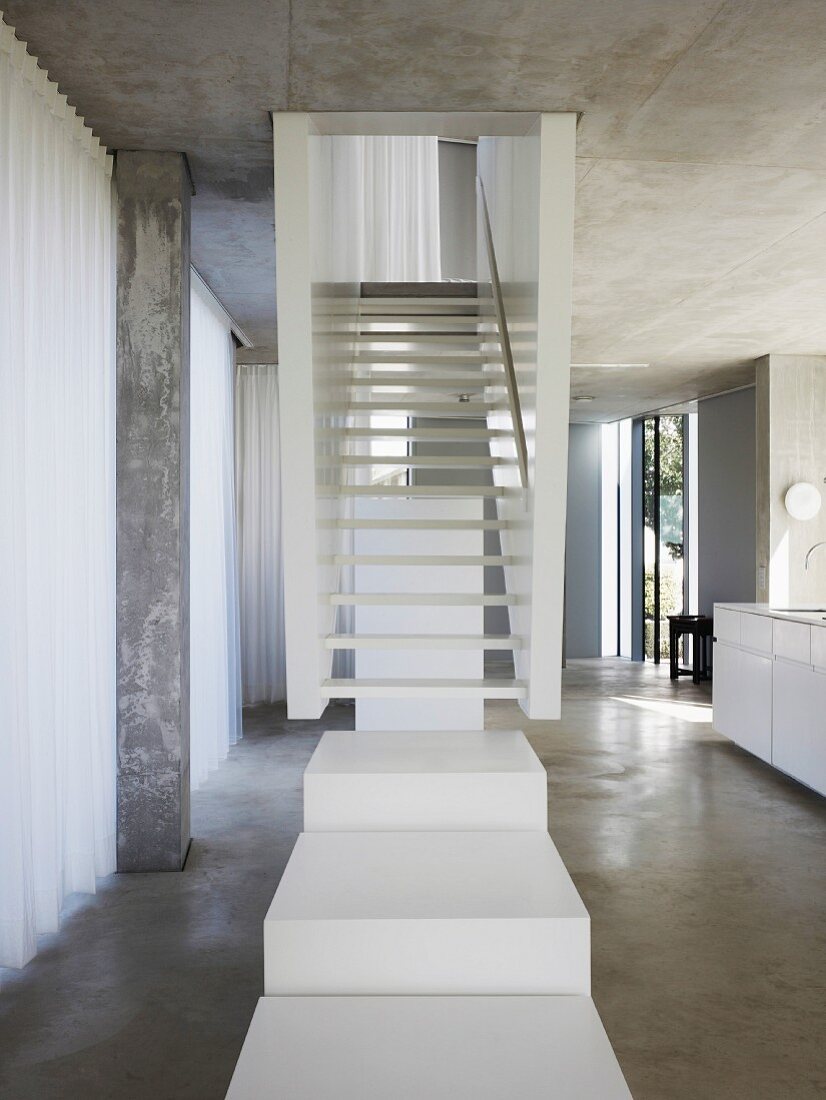 White stair landing in front of stairs in an open living room built of concrete