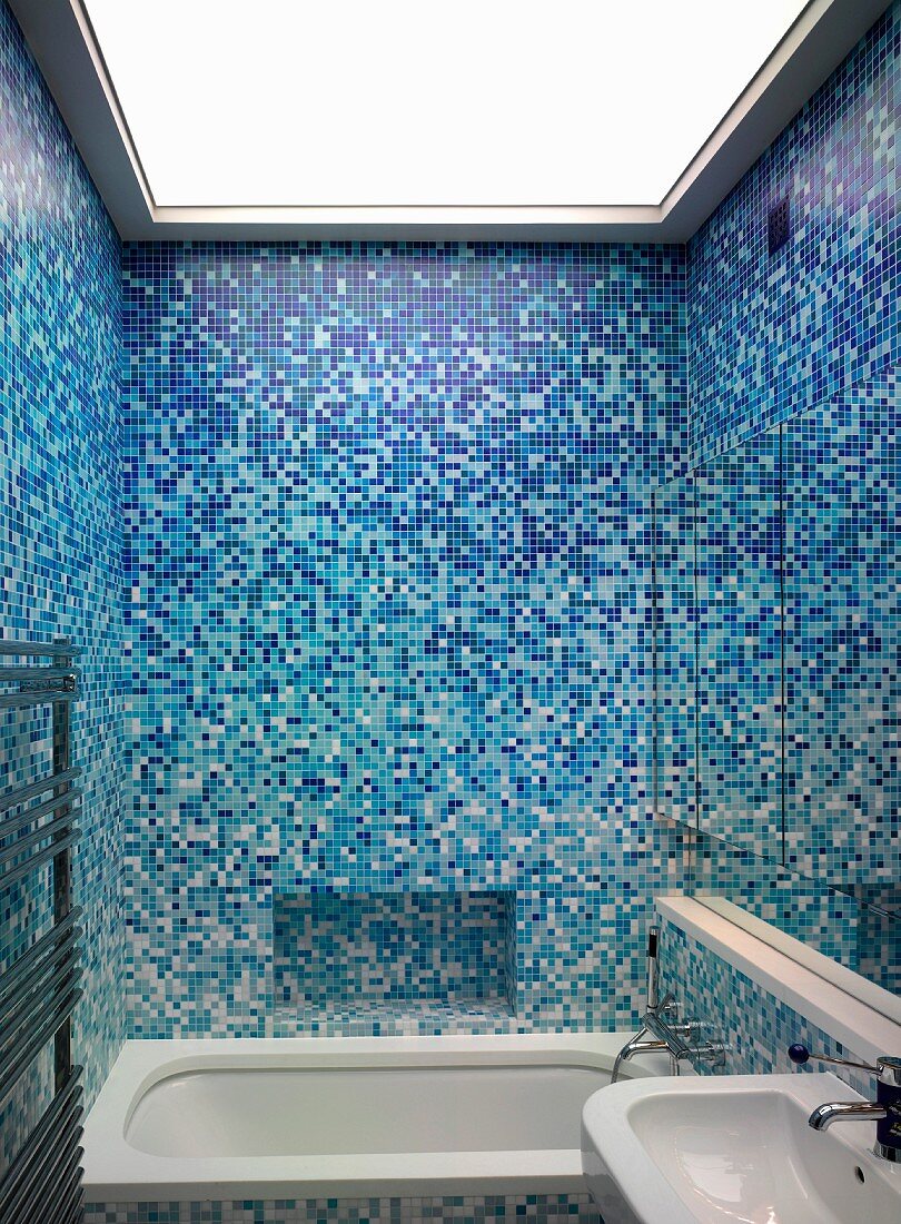 Bathroom with assorted blue mosaic tiles and bathtub under an illuminated ceiling