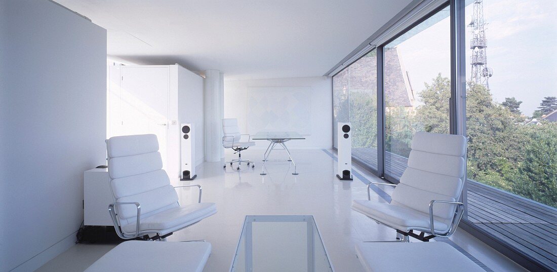 White living-dining room with white leather armchairs in front of a wall of windows