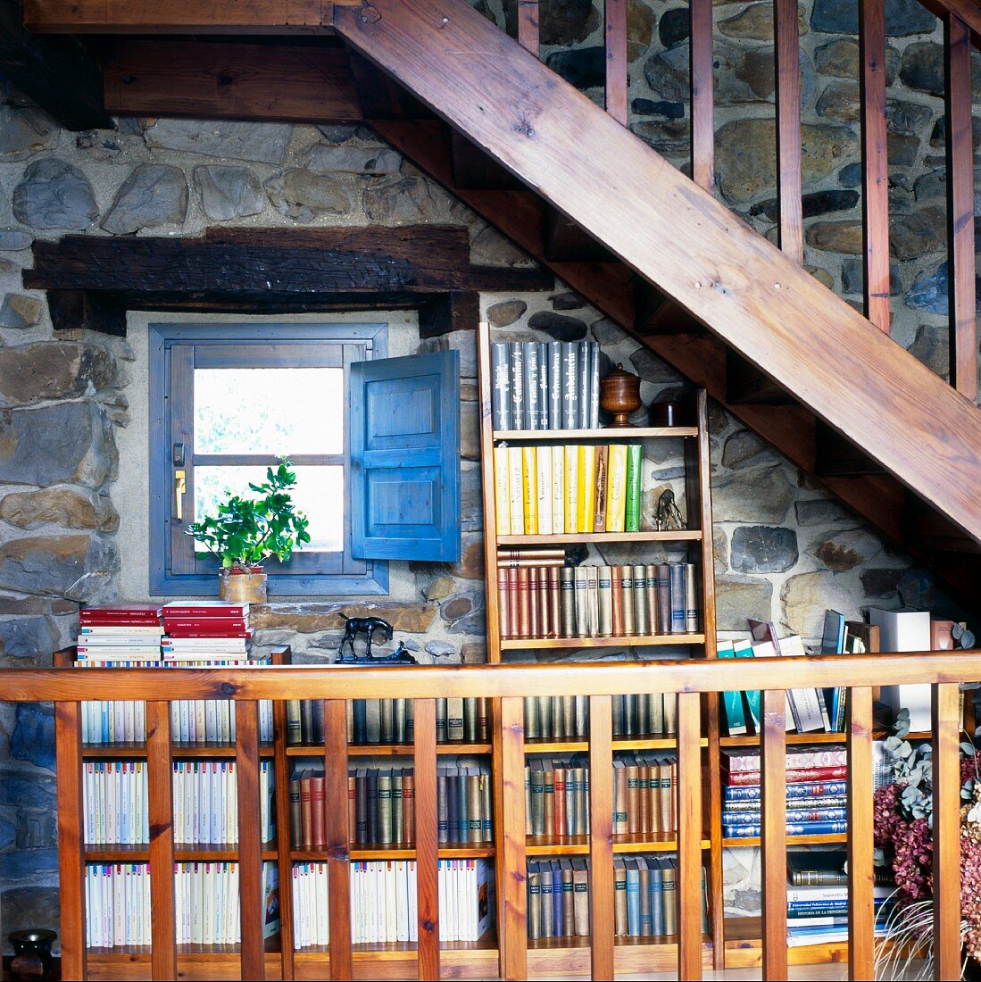 Wooden stairway above a mini-library on a natural stone wall of a country home