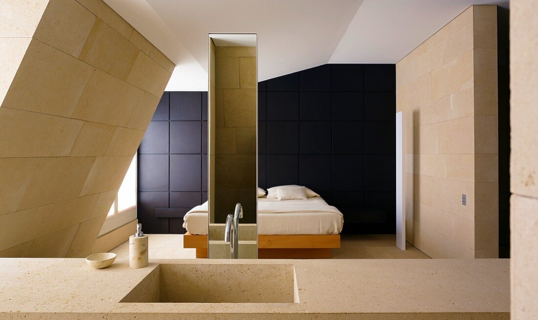 Stone wash basin in a bedroom with a bed in front of a wall clad in black wood