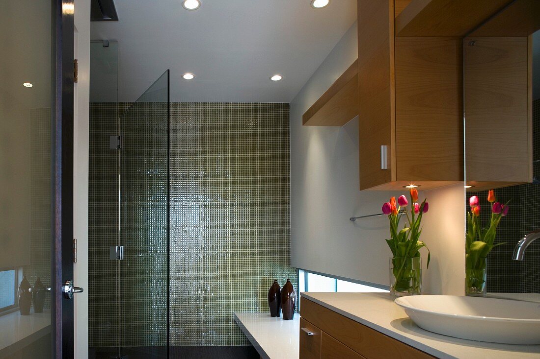 Modern bathroom with green tiles on the wall and an open glass door