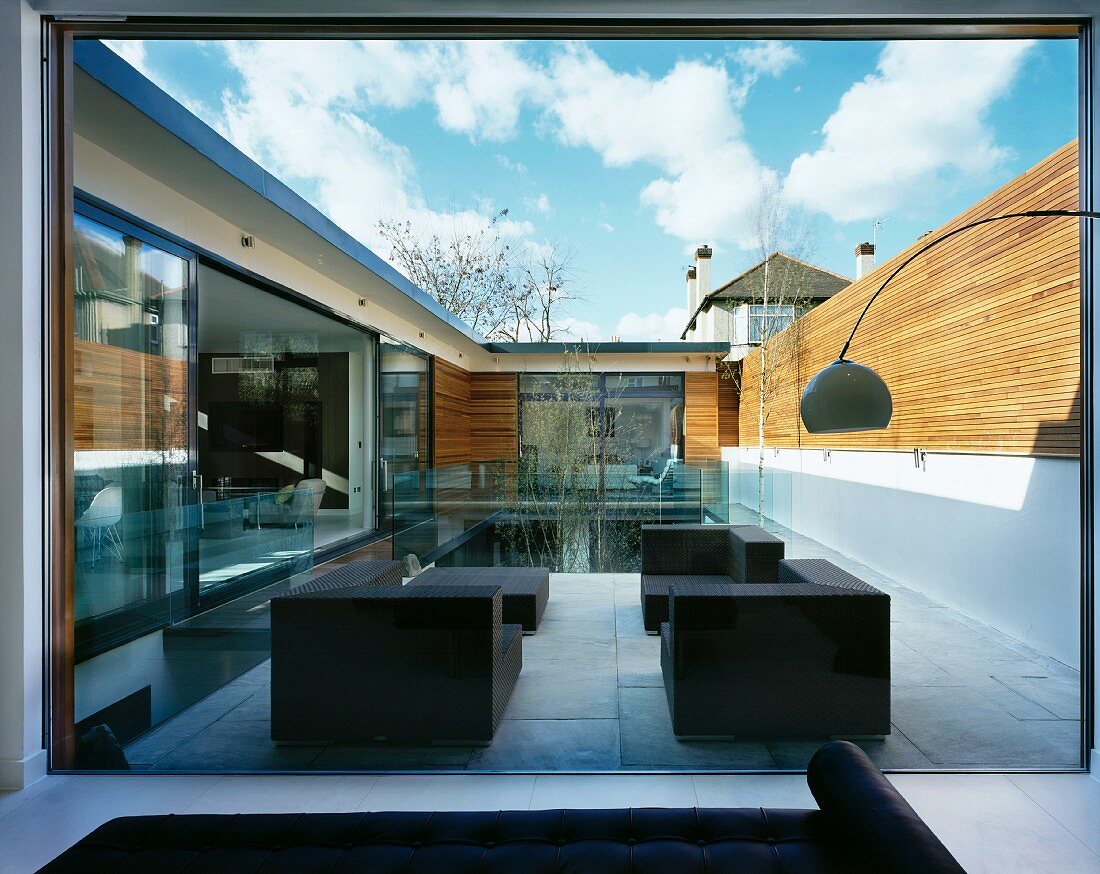 View through a bank of windows onto dark, cubic-shaped patio furniture in front of a pool in a contemporary courtyard